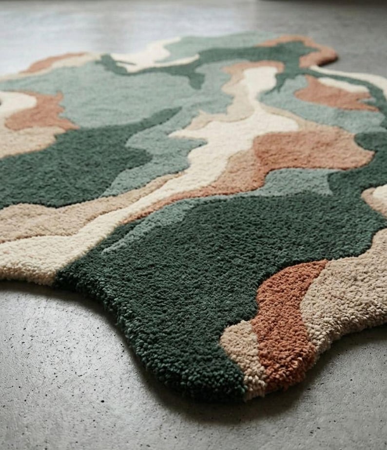 May include: An area rug with an irregular, organic shape featuring a tufted, high-pile texture. The design consists of abstract, flowing color blocks in shades of dark forest green, sage green, cream, and muted terracotta, creating a layered effect.