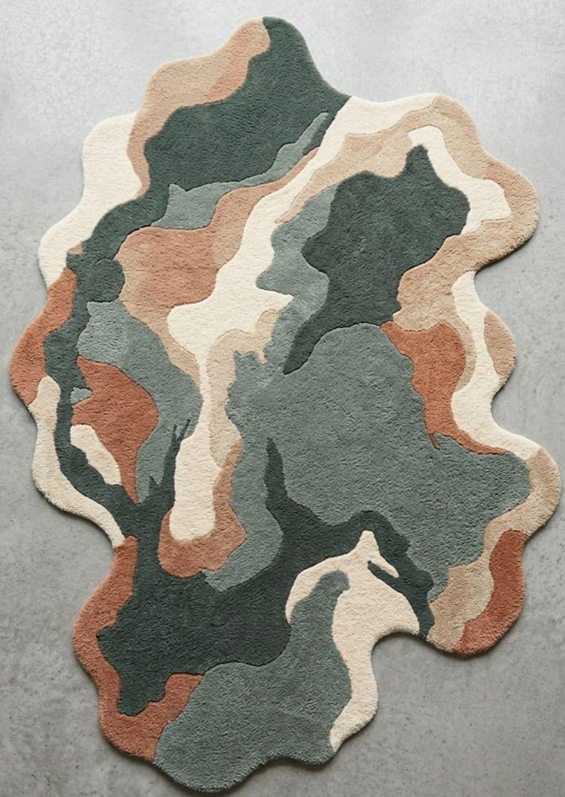 May include: An area rug with an irregular, organic shape featuring a tufted texture. The design consists of abstract, flowing color blocks in shades of dark forest green, muted sage, warm terracotta, and creamy off-white, creating a layered pattern.