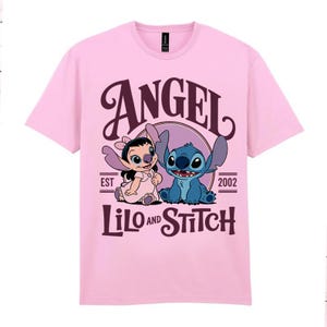 May include: A pale pink t-shirt with a graphic of Angel and Stitch from Lilo & Stitch. The design includes the word "ANGEL" in a decorative font above the characters, with "LILO AND STITCH" below. The text "EST 2002" is also included.