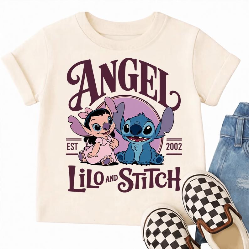 May include: Cream-coloured t-shirt featuring the characters Angel and Stitch from Lilo & Stitch. The design includes the word "ANGEL" above the characters, with "LILO AND STITCH" below. The shirt also has the text "EST 2002".
