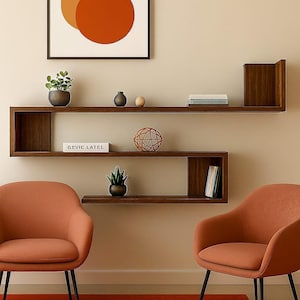 Könnte beinhalten: Moderne Wohnzimmereinrichtung mit einem geometrischen Wandregal aus dunklem Holz. Zwei orangefarbene Sessel mit schwarzen Beinen stehen auf einem orangefarbenen Teppich. Ein gerahmtes abstraktes Kunstwerk hängt über dem Regal. Das Regal zeigt Pflanzen, Bücher und dekorative Objekte.