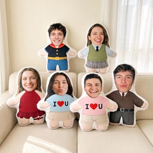 May include: Six custom-shaped plush pillows featuring printed photographic faces of different individuals on cartoon-style bodies wearing various outfits, including a sailor suit, a green sweater vest, a red dress, and shirts with I heart U text.