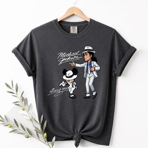 May include: Dark gray t-shirt featuring a cartoon illustration of Michael Jackson and Mickey Mouse in matching outfits. The text "Michael Jackson" and "Mickey Mouse" are written in a cursive font.