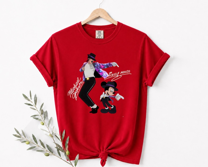 Puede incluir: Camiseta roja con un gr&aacute;fico de Michael Jackson y Mickey Mouse. El dise&ntilde;o muestra a Michael Jackson con sombrero y pantal&oacute;n negros con una chaqueta colorida, y a Mickey Mouse con un atuendo similar. Las palabras "Michael Jackson" y "Mickey Mouse" est&aacute;n escritas en cursiva.