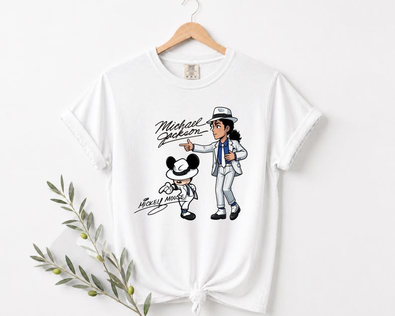 May include: White t-shirt featuring a cartoon illustration of Michael Jackson and Mickey Mouse. Michael Jackson is depicted in a white suit and hat, pointing. Mickey Mouse is also in a white suit and hat. The words "Michael Jackson" and "Mickey Mouse" are written in cursive.