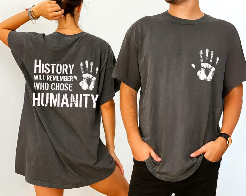May include: Dark gray t-shirts with white handprint graphics. One shirt has a handprint on the front and the text "HISTORY WILL REMEMBER WHO CHOSE HUMANITY" on the back. The shirts are short-sleeved and have a vintage, worn look.
