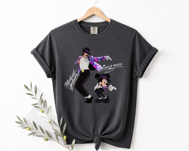 Puede incluir: Camiseta gris oscuro con un dise&ntilde;o de Michael Jackson y Mickey Mouse. El dise&ntilde;o incluye el texto "Michael Jackson" y "Mickey Mouse". La camiseta est&aacute; colgada en una percha de madera. La camiseta es de color gris oscuro.