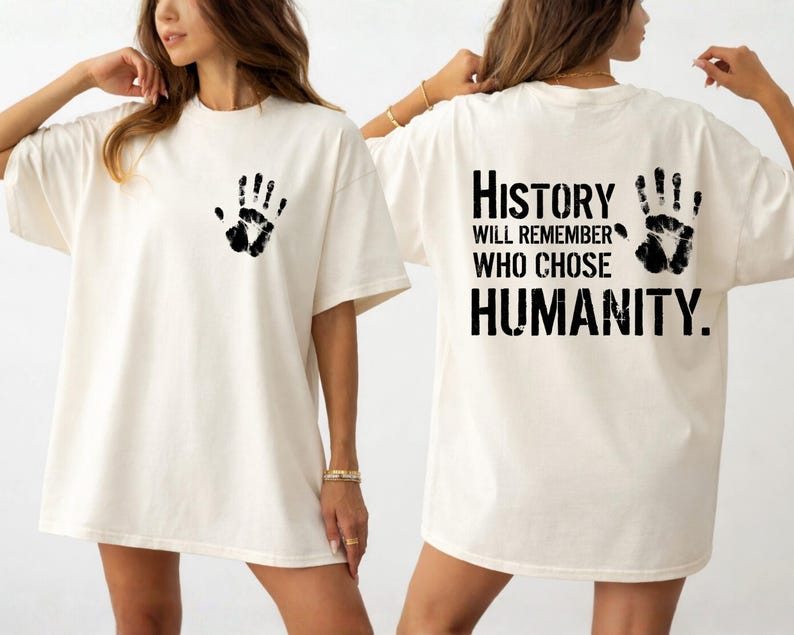 May include: Cream-colored t-shirt with a black handprint on the front and back. The back of the shirt features the text "History will remember who chose humanity."