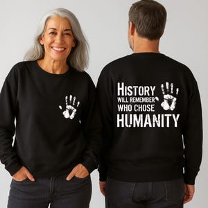 May include: Black sweatshirt with a white handprint on the front and the text "History Will Remember Who Chose Humanity" on the back. The sweatshirt is a crew neck style.