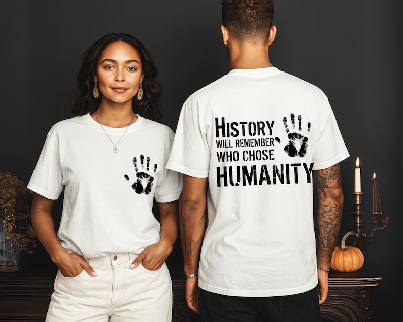 May include: White t-shirts with a black handprint design. One shirt has a handprint on the front, and the other has a handprint and the text "History will remember who chose humanity".
