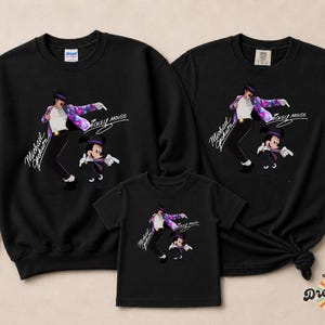 Puede incluir: Sudaderas y camisetas negras con un gr&aacute;fico de Michael Jackson y Mickey Mouse. El dise&ntilde;o incluye el texto "Michael Jackson" y "Mickey Mouse". La imagen muestra una sudadera y dos camisetas.