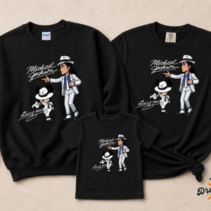 May include: Black sweatshirts and t-shirts featuring a cartoon illustration of Michael Jackson and Mickey Mouse. The design includes the text "Michael Jackson" and "Mickey Mouse" in a script font. The apparel is suitable for a family.