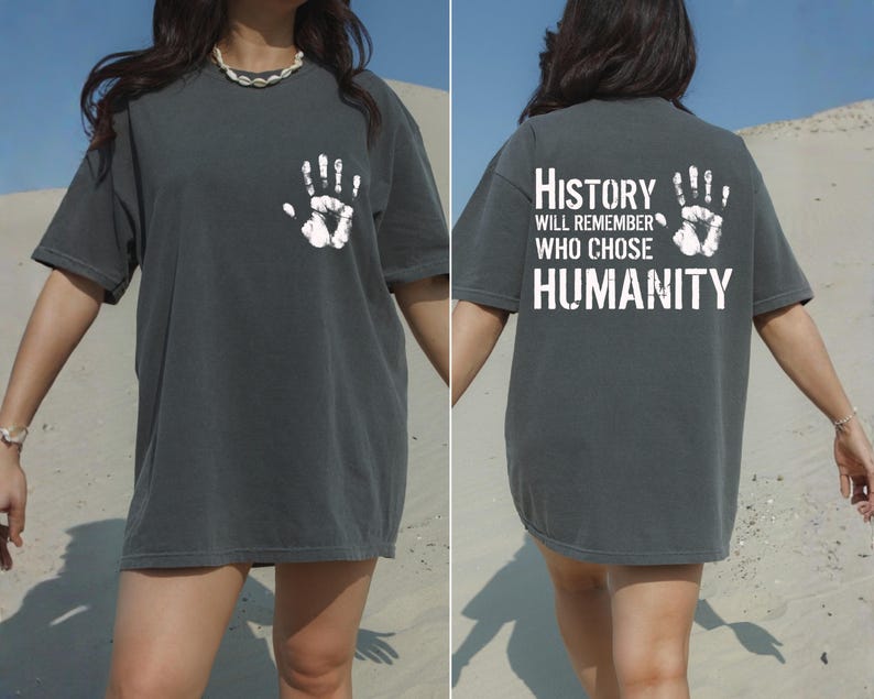 May include: Dark gray t-shirt with a white handprint on the front and back. The back of the shirt features the text "History will remember who chose humanity" in white block letters. The shirt is a casual, oversized fit.