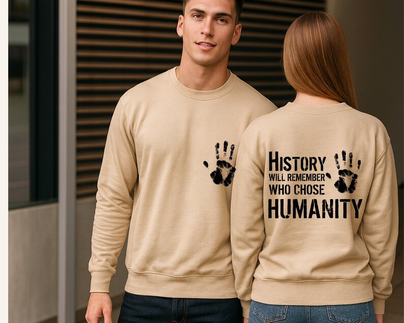May include: Beige sweatshirts with black handprint designs. One sweatshirt has a handprint on the front pocket, the other has two handprints and the text "History will remember who chose humanity" on the back.