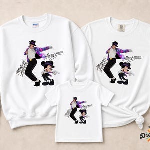 Unisex t-shirt, sweatshirt, hoodie, and baby bodysuit featuring a Michael Jackson and Mickey Mouse dancing graphic with galaxy jacket details and pop icon theme.
