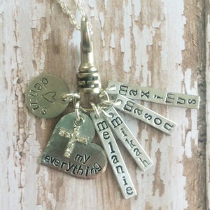 May include: A silver necklace with a heart charm that says "my everything" and a cross charm with rhinestones. The necklace also has several charms with names on them, including "Maximus", "Mason", "Melanie", and "Micah".