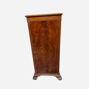 Può includere: Un mobile alto rettangolare in legno con una ricca finitura in mogano marrone scuro e un prominente motivo a venature ovali sulla porta anteriore. Il mobile è accentuato da sottili linee di intarsio chiare e poggia su quattro piedi intagliati.