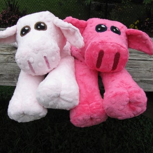 May include: Two plush animal toys, one light pink and one bright pink, resembling pigs. Each has large, dark eyes, floppy ears, and long legs. The toys are made of soft, textured fabric and are lying on a weathered wooden surface.