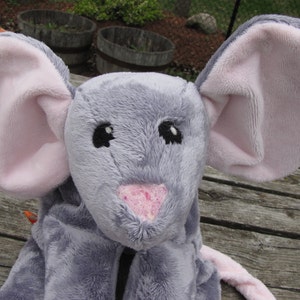 May include: A gray plush mouse with pink ears and a pink nose. The mouse has black eyes and a stitched smile.