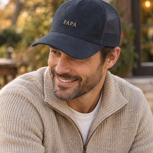 Puede incluir: Una gorra de béisbol azul marino con un panel frontal estructurado y parte trasera de malla. La parte delantera de la gorra presenta la palabra PAPA bordada en hilo color canela claro. La gorra tiene una visera curva y un botón superior.