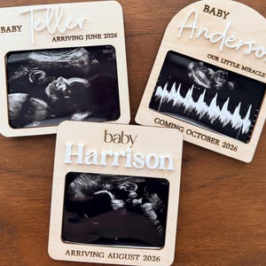 May include: Three light-colored wooden plaques for ultrasound photos. One square plaque reads BABY TELLER ARRIVING JUNE 2026, one arched plaque reads BABY Anderson OUR LITTLE MIRACLE COMING OCTOBER 2026, and one square plaque reads baby Harrison ARRIVING AUGUST 2026.