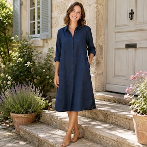 May include: A dark blue midi-length shirt dress featuring a classic collar, long sleeves with buttoned cuffs, and a full-length front button placket. The garment is crafted from a textured fabric and has a relaxed, straight-cut silhouette.