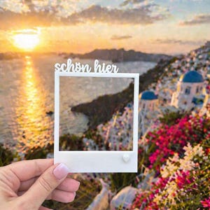 Könnte beinhalten: Ein weißer Fotorahmen mit der Aufschrift "schön hier" wird vor einem malerischen Hintergrund eines Sonnenuntergangs über dem Meer und einem Dorf gehalten. Der Rahmen hat ein kleines Herzdetail. Die Szene umfasst bunte Blumen.