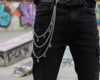 May include: Silver chain with star charms attached to a black belt and black jeans. The chain hangs in three strands, each with multiple star-shaped charms. The jeans have a distressed look.