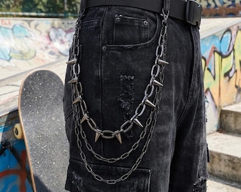 May include: Black denim pants with distressed details and a black belt. A silver chain with cone-shaped spikes hangs from the belt loop. The pants have a cargo pocket and are worn with a black belt.