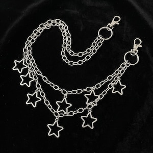 May include: Silver-toned chain belt with multiple strands and star-shaped charms. The belt features two lobster claw clasps and is designed to be worn around the waist or hips. The chains and charms are made of a shiny, metallic material.