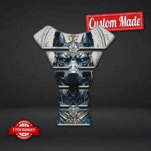 Puede incluir: Un protector de depósito de motocicleta con una ilustración detallada de una criatura parecida a un lobo con ojos azules brillantes. El diseño es predominantemente plateado y azul, con las palabras "Custom Made" en rojo.