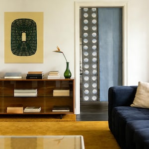 Könnte beinhalten: Ein modernes Wohnzimmer mit einem senfgelben Teppich, einem dunkelblauen Sofa und einem Holzschrank. Ein großes abstraktes Gemälde hängt an der Wand. Eine grüne Vase hält eine Blume. Ein Türrahmen führt zu einem Raum mit einem gemusterten Vorhang.
