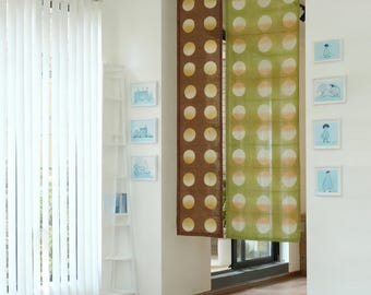 Puede incluir: Vista interior con una persiana vertical blanca y dos cortinas decorativas. Una es marrón con círculos amarillos, la otra es verde con círculos melocotón. Pequeñas imágenes enmarcadas cuelgan de la pared y se ve una estantería blanca.