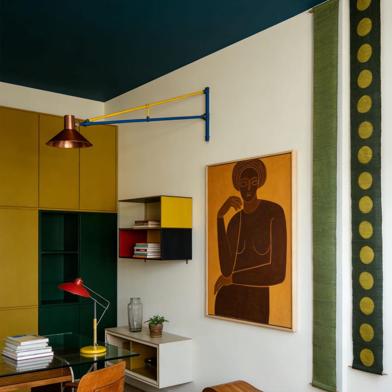 May include: Interior design with a modern aesthetic. A copper-coloured wall lamp is mounted on the wall. A framed painting of a woman hangs on the wall. A red desk lamp sits on a glass desk. The colour scheme is yellow and green.