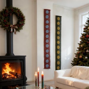 May include: A festive living room with a fireplace, Christmas tree, and white sofa. Two vertical wall hangings with large polka dots in blue and yellow are displayed. A green wreath with red berries hangs above the fireplace.