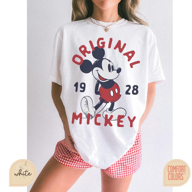 May include: White t-shirt featuring a graphic of Mickey Mouse with the words "ORIGINAL MICKEY" in red and navy blue. The year "1928" is also printed on the shirt. The shirt is paired with red and white checkered shorts.