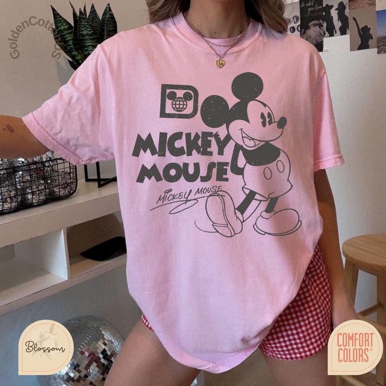 Puede incluir: Camiseta rosa claro con un dise&ntilde;o vintage de Mickey Mouse y la frase "Mickey Mouse". El dise&ntilde;o incluye un icono de globo. La camiseta es de la marca Comfort Colors, con cuello redondo y mangas cortas.