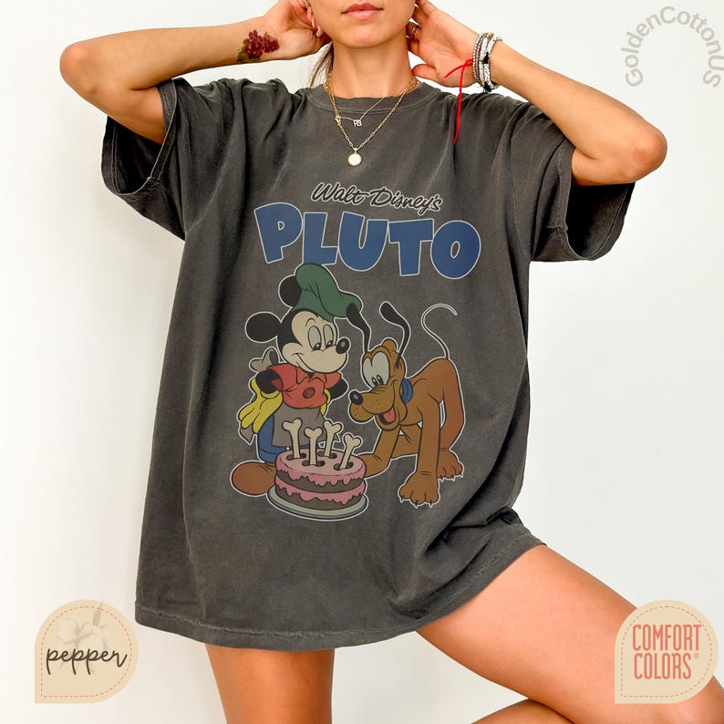 Puede incluir: Camiseta gris oscuro con un dise&ntilde;o de Mickey Mouse y Pluto celebrando con una tarta. El texto "Walt Disney's PLUTO" est&aacute; impreso en azul sobre los personajes. Marca Comfort Colors.