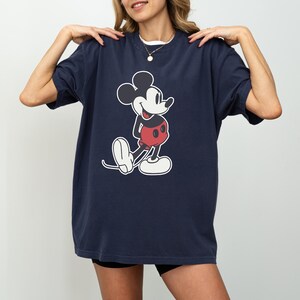 May include: Navy blue t-shirt featuring a classic Mickey Mouse graphic. The cartoon character is depicted in black, white, and red. The shirt has a relaxed fit and short sleeves, suitable for casual wear.
