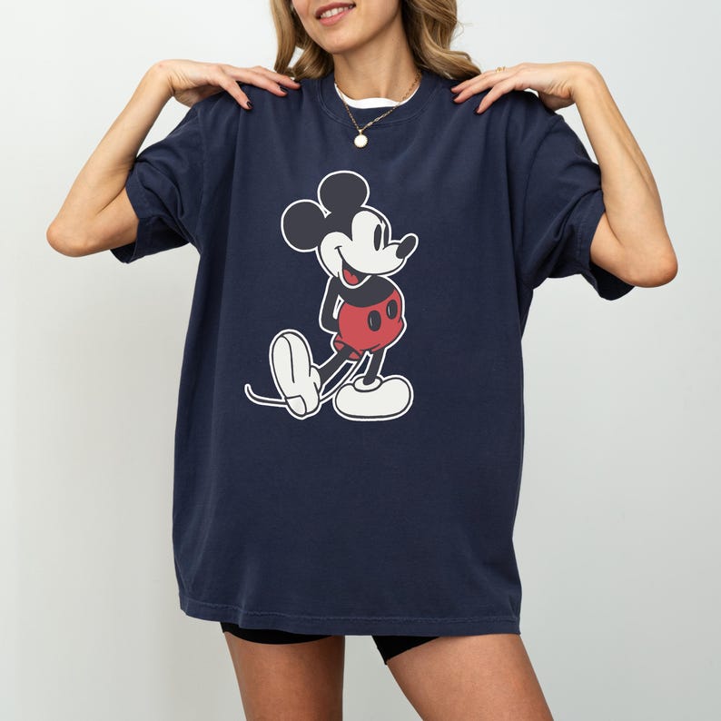 May include: Navy blue t-shirt featuring a classic Mickey Mouse graphic. The cartoon character is depicted in black, white, and red. The shirt has a relaxed fit and short sleeves, suitable for casual wear.