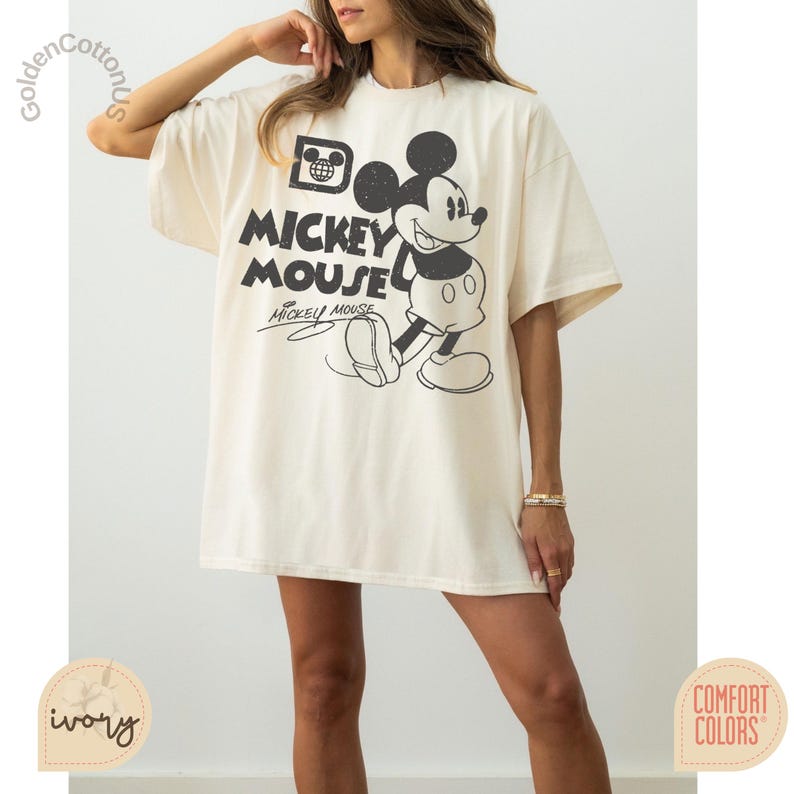 Puede incluir: Camiseta de gran tama&ntilde;o de color marfil con un gr&aacute;fico en blanco y negro de Mickey Mouse. El dise&ntilde;o incluye las palabras "Mickey Mouse" en negrita, con la firma de Mickey Mouse debajo. La camiseta es de la marca Comfort Colors.