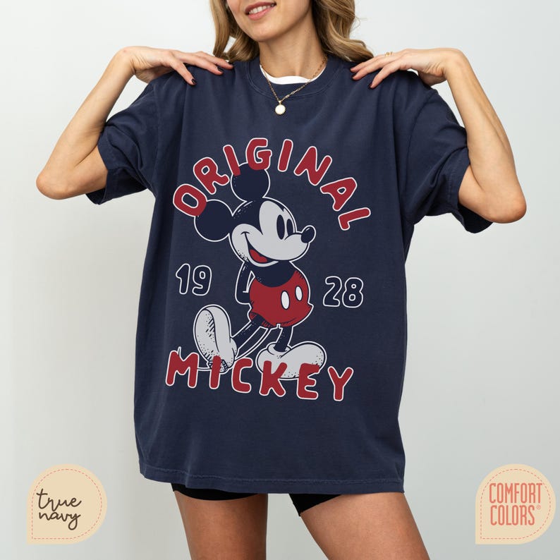 May include: Navy blue t-shirt featuring a classic Mickey Mouse graphic. The design includes the word "ORIGINAL" in red, the year "1928", and the name "MICKEY". The shirt is a Comfort Colors brand.