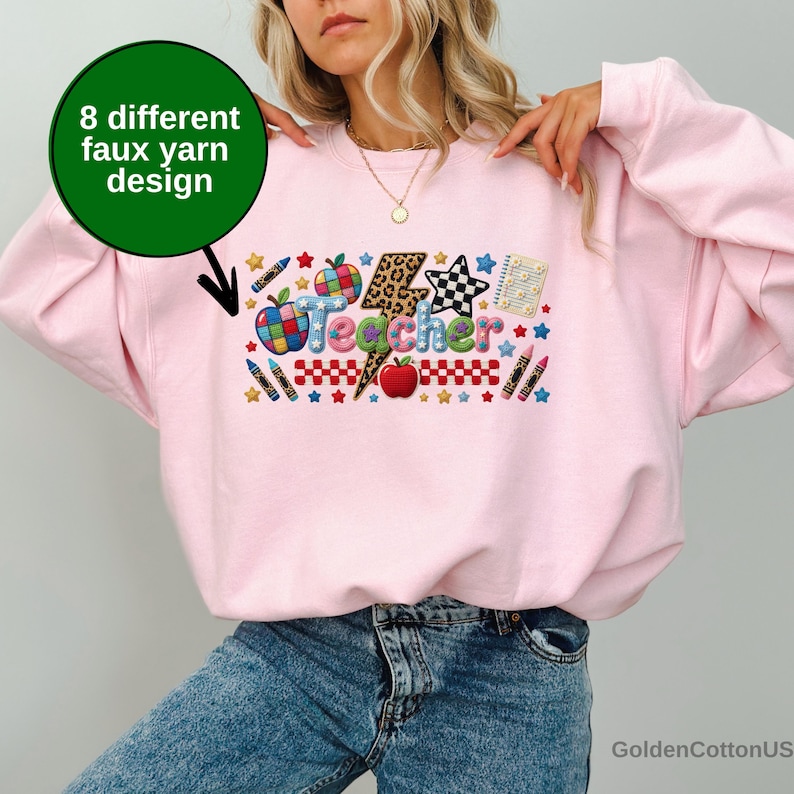Puede incluir: Una sudadera rosa claro con un gr&aacute;fico colorido que muestra la palabra Teacher en un estilo de hilo falso texturizado. El dise&ntilde;o incluye un rayo con estampado de leopardo, una manzana roja, crayones, estrellas y un patr&oacute;n de cuadros. Un c&iacute;rculo verde con texto.