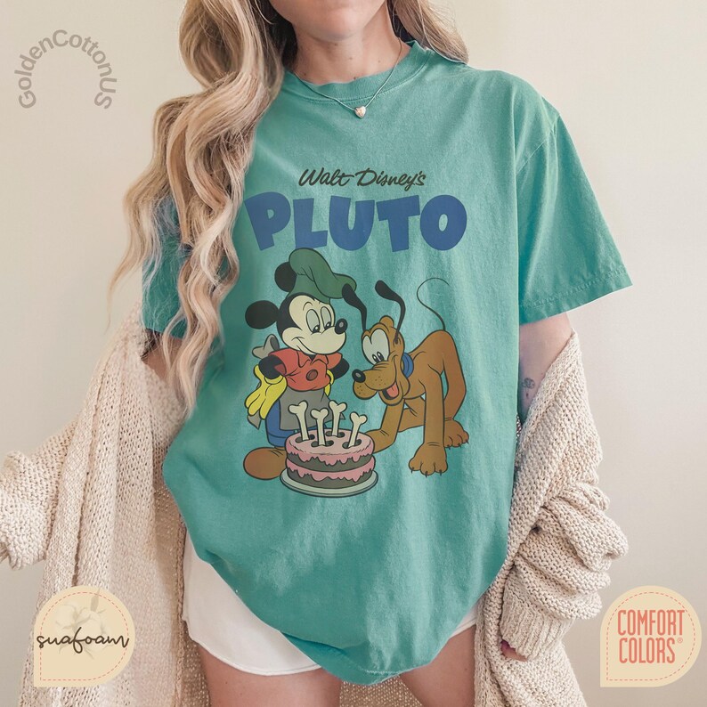 Puede incluir: Camiseta de color turquesa con un gr&aacute;fico de Mickey Mouse y Pluto con una tarta. El texto "Walt Disney's PLUTO" est&aacute; impreso en azul. La camiseta es de la marca Comfort Colors.