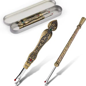 Könnte beinhalten: Antike Nahttrenner aus Messing mit aufwendigen floralen Designs und Schmuckakzenten. Einer wird mit einem dekorativen Griff und der andere in einer silbernen Metallbox gezeigt. Die Nahttrenner haben eine silberne Klinge mit roter Sicherheitskugel.