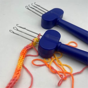 May include: Two blue plastic knitting tools with metal hooks. One tool has four hooks, and the other has three hooks. The three-hook tool is actively working on a strand of variegated yarn in shades of pink, orange, and yellow, creating a braided cord.
