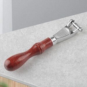 May include: A kitchen tool featuring a polished silver-colored metal head with a textured grip area and a smooth, dark reddish-brown wooden handle. The metal component includes a small, rotating cylindrical bar at the tip for peeling vegetables.