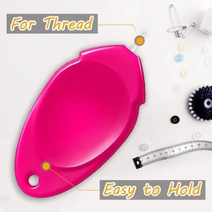 Puede incluir: Un portahilos rosa brillante con el texto "For Thread" y "Easy to Hold". La imagen también muestra varios accesorios de costura, como botones, imperdibles y una cinta métrica.