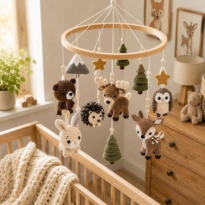 May include: A wooden baby mobile featuring crocheted woodland creatures, including a bear, deer, owl, and rabbit. The mobile also includes crocheted trees, stars, and a mountain, all suspended from a wooden ring.