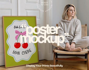 Può includere: Un poster incorniciato con sfondo verde presenta un design stravagante di due ciliegie rosse, un fiocco rosa e le parole "Ooh La La" e "Mon Cherie". Il poster è in una stanza con una donna seduta su una sedia.